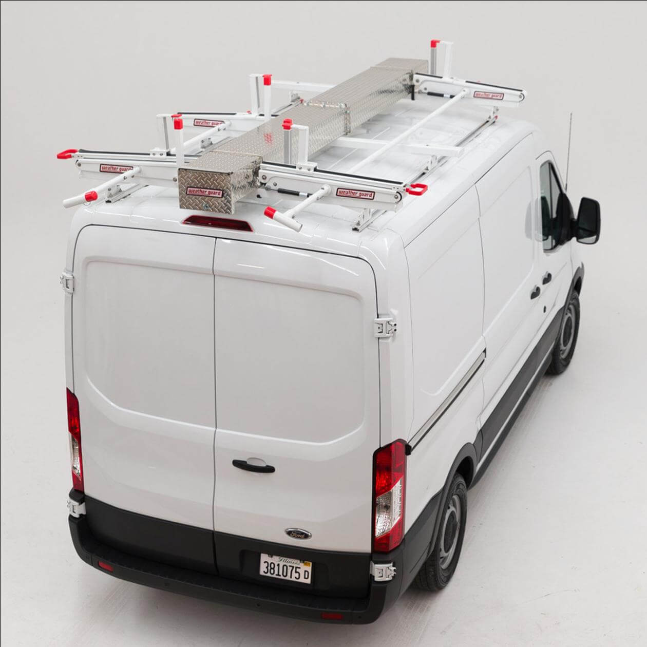 A white van with a roof rack system equipped with ladders and a metal storage box, viewed from the rear angle, against a plain background.