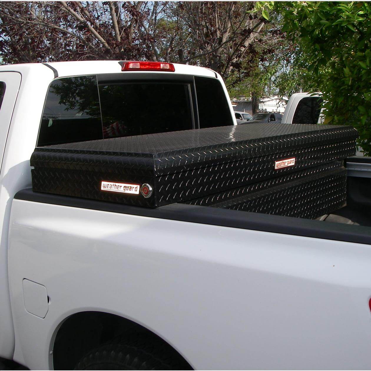 A white pickup truck with a black diamond-plate toolbox mounted in the bed.