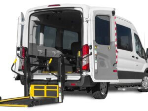 White Ford Paratransit van with rear doors open, showcasing a deployed wheelchair lift.